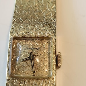 May include: A gold-toned Longines wristwatch with a square face and a textured band.