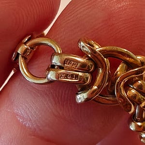 May include: Close-up of a gold chain bracelet with a clasp that has the inscription "B.G.I."