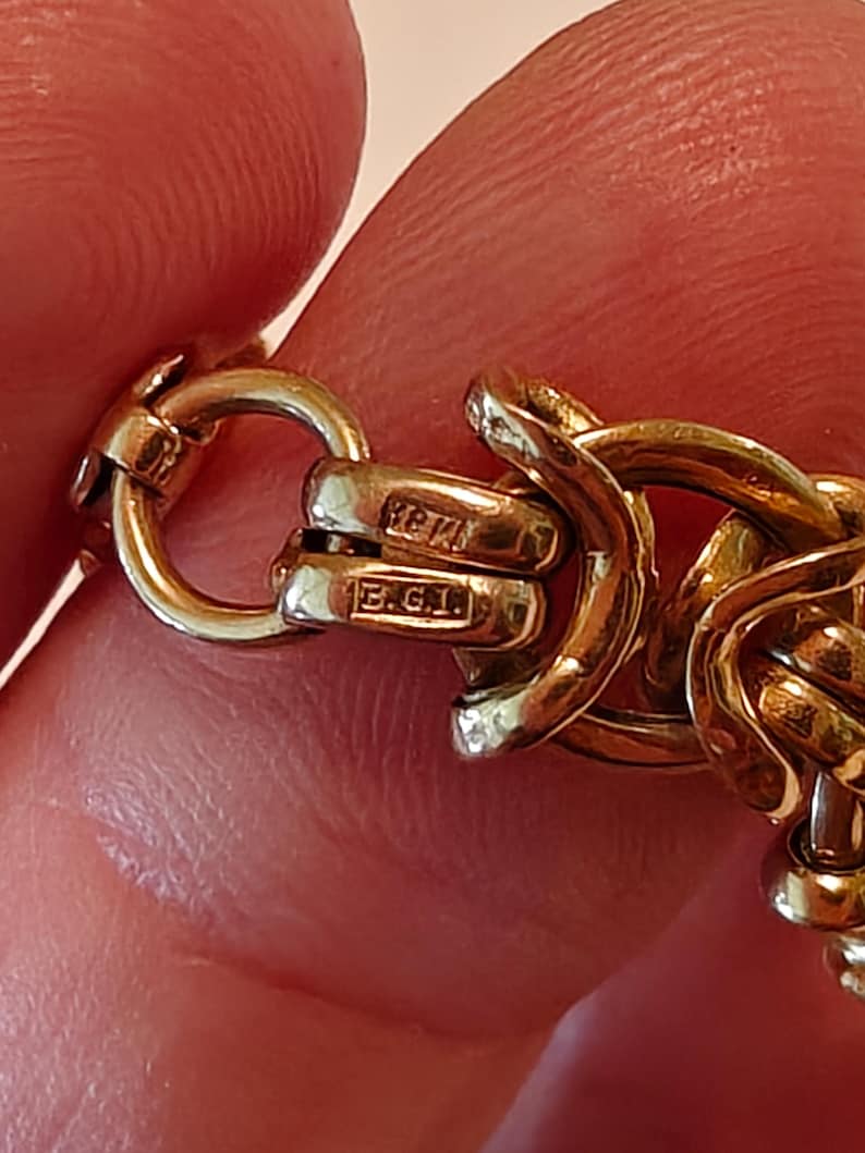 May include: Close-up of a gold chain bracelet with a clasp that has the inscription "B.G.I."