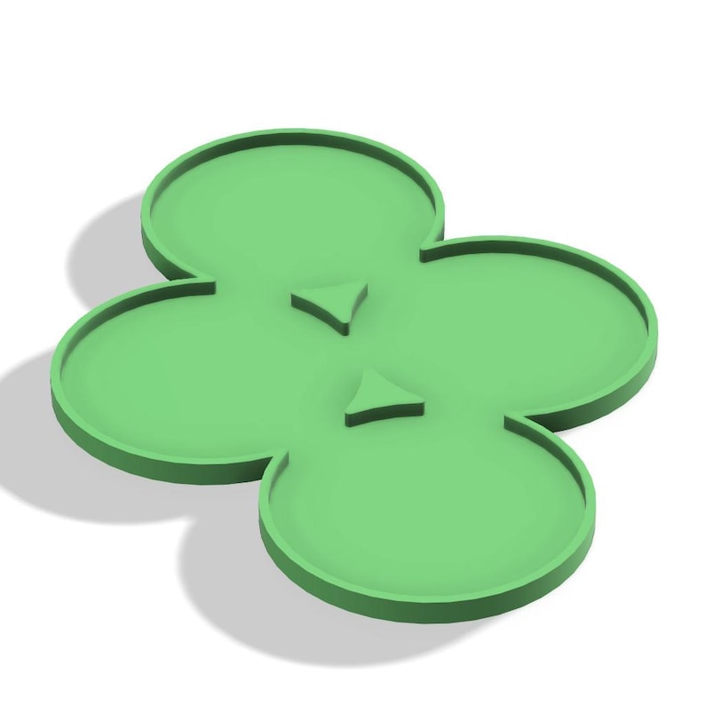 May include: A light green, four-leaf clover-shaped tray with raised edges and two small, triangular accents. The tray is made of a solid material and casts a shadow on a white surface.