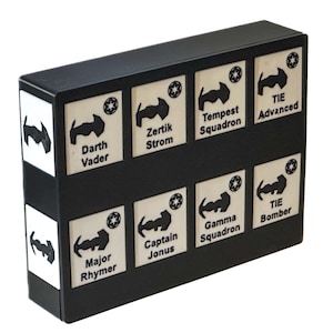 Könnte beinhalten: Eine schwarze Box mit acht weißen Quadraten, jedes mit einem schwarzen Stern und einem schwarzen Bild eines Raumschiffs. Der Text auf den Quadraten lautet: Darth Vader, Zertik Strom, Tempest Squadron, TIE Advanced, Major Rhymer, Captain Jonus, Gamma Squadron, TIE Bomber.