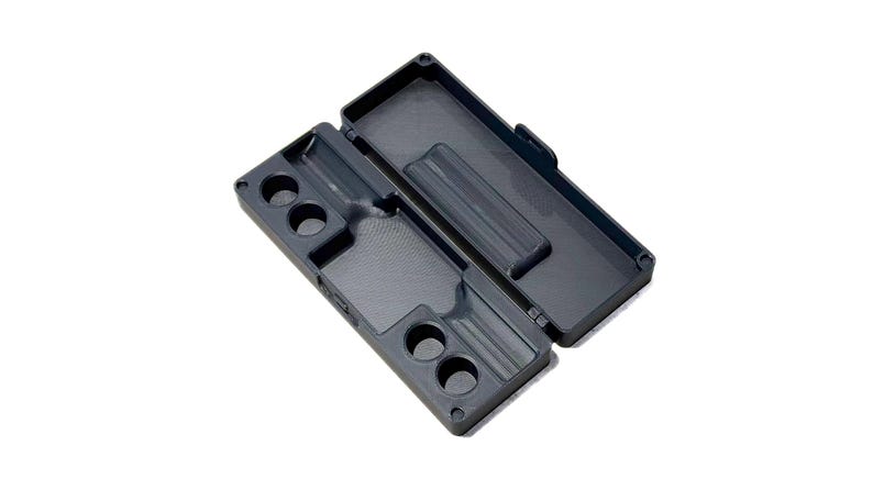 May include: A dark gray rectangular storage case with a hinged lid, featuring a molded interior with four circular cutouts on one side and a long recessed channel, designed for organizing small items within its structured, partitioned compartments.