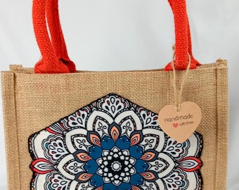 May include: A brown jute tote bag with orange handles. The bag features a colorful mandala design and a brown heart-shaped tag that reads "Handmade with love".