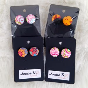 Puede incluir: Cuatro pares de pendientes de botón de tela coloridos que se muestran en tarjetas negras con el texto "Louise D. Handmade".