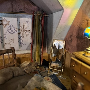May include: A dollhouse bedroom with a bed, dresser, and a broken mirror. The walls are painted a dark brown color and have white markings. The window has a striped curtain and a view of a cloudy sky.