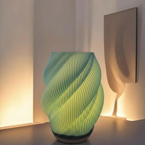 Op de afbeelding: Een turquoise, spiraalvormige vaas met verticale ribbels. De vaas heeft een getextureerd oppervlak en een donkere basis. De binnenkant gloeit met een zacht geel licht, wat een contrast creëert met de koele tinten van de buitenkant. Het ontwerp is modern en sculpturaal.