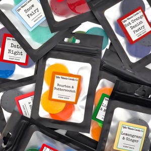 May include: An assortment of wax melts in various colours and scents, packaged in clear plastic bags with black labels. The labels feature the company name "Little Rituals Candle Co." and the scent names, such as "Snow Fairy", "Date Night", "Bourbon & Butterscotch", "Hot Orange Danish Pastry", "Lemongrass & Ginger", and "Lime & Mint".