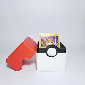 May include: A red and white Pokemon card deck box with a black lid. The lid is open and a Pokemon card featuring Raichu is visible inside. The card has a gold border and the text "Raichu 120+ ".
