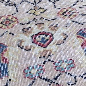 May include: Close-up of a beige rug with an intricate pattern. The design features floral and geometric shapes in red, blue, yellow, and black. The rug has a vintage, handcrafted appearance.