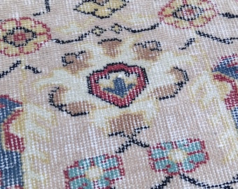 May include: Close-up of a beige rug with an intricate pattern. The design features floral and geometric shapes in red, blue, yellow, and black. The rug has a vintage, handcrafted appearance.
