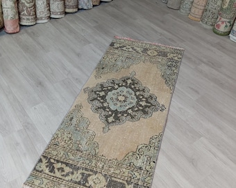 Puede incluir: Una alfombra de pasillo beige claro con un diseño intrincado descolorido en tonos de azul, verde y negro. La alfombra tiene un aspecto desgastado y vintage y presenta un medallón central con un motivo floral.
