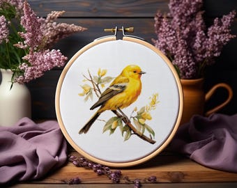 May include: A circular wooden embroidery hoop containing white fabric with a printed illustration of a bright yellow bird perched on a thin brown branch with small green leaves and yellow flowers, secured by a metal tension screw.