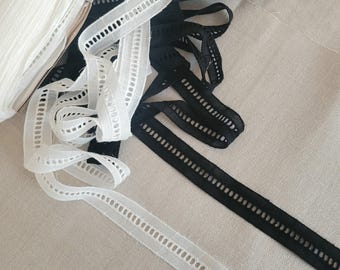 May include: Close-up of white and black decorative ribbon. The ribbons are thin, with a series of small, evenly spaced holes running down the center. The white ribbon is rolled up on the left, while the black and white ribbons are scattered.