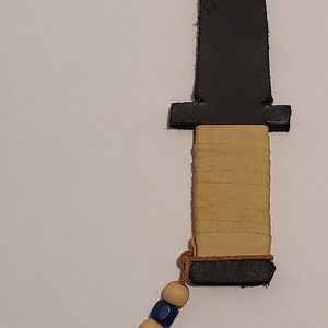 May include: A black leather knife with a tan leather handle and a brown leather cord with wooden and blue beads.