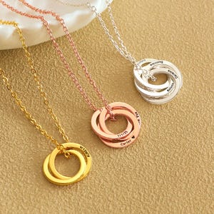 May include: Four gold, silver and rose gold necklaces with interlocking rings. Each ring is engraved with names and a heart symbol.