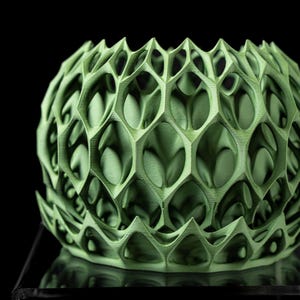 May include: A green 3D printed geometric vase with a honeycomb pattern. The vase is made of plastic and has a smooth, matte finish.