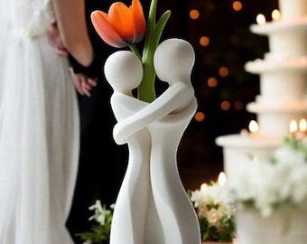 May include: White ceramic sculpture of two figures embracing, holding a single orange tulip. The sculpture is a wedding or anniversary gift.