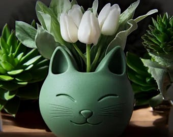 May include: A green ceramic cat planter with a smiling face and whiskers. The planter is filled with white tulips.