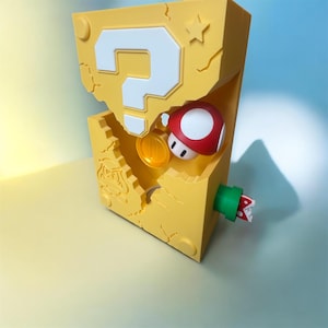 Pode incluir: Um bloco amarelo com um ponto de interroga&ccedil;&atilde;o branco, um cogumelo vermelho e branco e uma moeda de ouro. Um cano verde com uma planta vermelha e branca emerge da lateral. O bloco tem um design rachado.