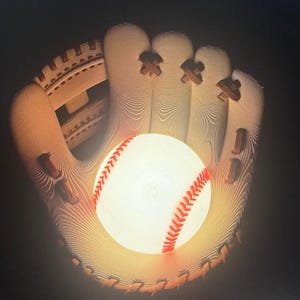 May include: A baseball glove cradles a glowing baseball. The glove is tan with brown stitching and accents. The baseball is white with red stitching. The image is set against a dark background.