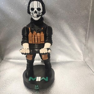 K&ouml;nnte beinhalten: Figur einer Figur aus dem Videospiel Call of Duty: Modern Warfare II. Die Figur tr&auml;gt ein schwarzes Outfit, ein Headset und eine Totenkopfmaske. Die Basis ist schwarz mit dem Text "MWII" in Wei&szlig; und Gr&uuml;n.