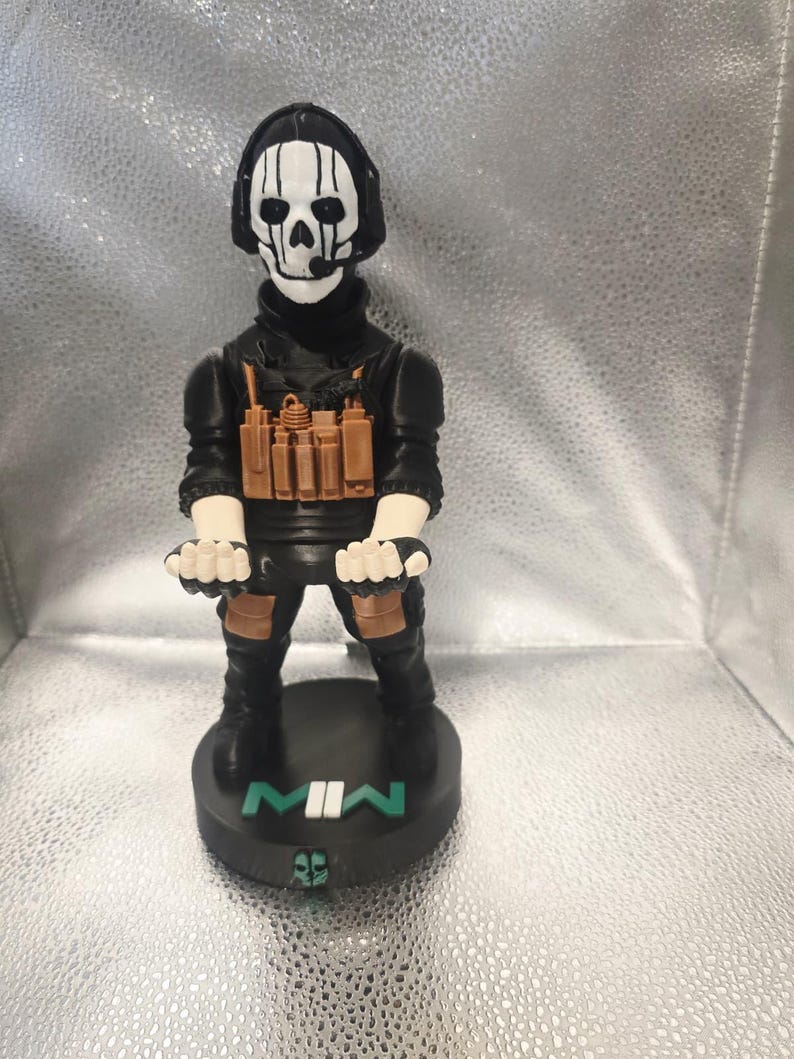 K&ouml;nnte beinhalten: Figur einer Figur aus dem Videospiel Call of Duty: Modern Warfare II. Die Figur tr&auml;gt ein schwarzes Outfit, ein Headset und eine Totenkopfmaske. Die Basis ist schwarz mit dem Text "MWII" in Wei&szlig; und Gr&uuml;n.