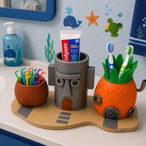 May include: A bathroom organizer set featuring a brown textured cup for floss picks, a gray cylindrical head-shaped container holding a tube of Colgate Kids Cavity Protection toothpaste, and an orange pineapple-shaped holder with two toothbrushes.
