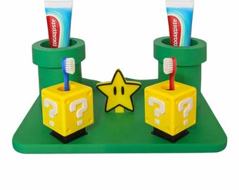 May include: A green platform with two green pipe-shaped holders for toothpaste tubes. Two yellow question mark boxes hold toothbrushes, and a yellow star is in the center. The toothpaste tubes are blue and white.
