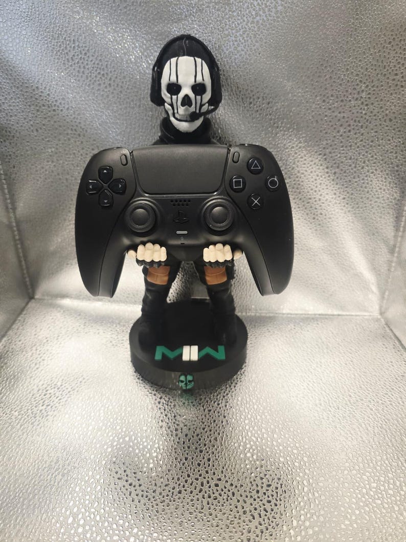 K&ouml;nnte beinhalten: Schwarze Gaming-Controller-Figur mit einem sch&auml;delgesichtigen Kopf und einem schwarzen Sockel. Der Controller hat Tasten und ein Steuerkreuz. Der Sockel tr&auml;gt die Buchstaben "MWII" in Wei&szlig; und Gr&uuml;n. Die Figur ist ein Sammlerst&uuml;ck.