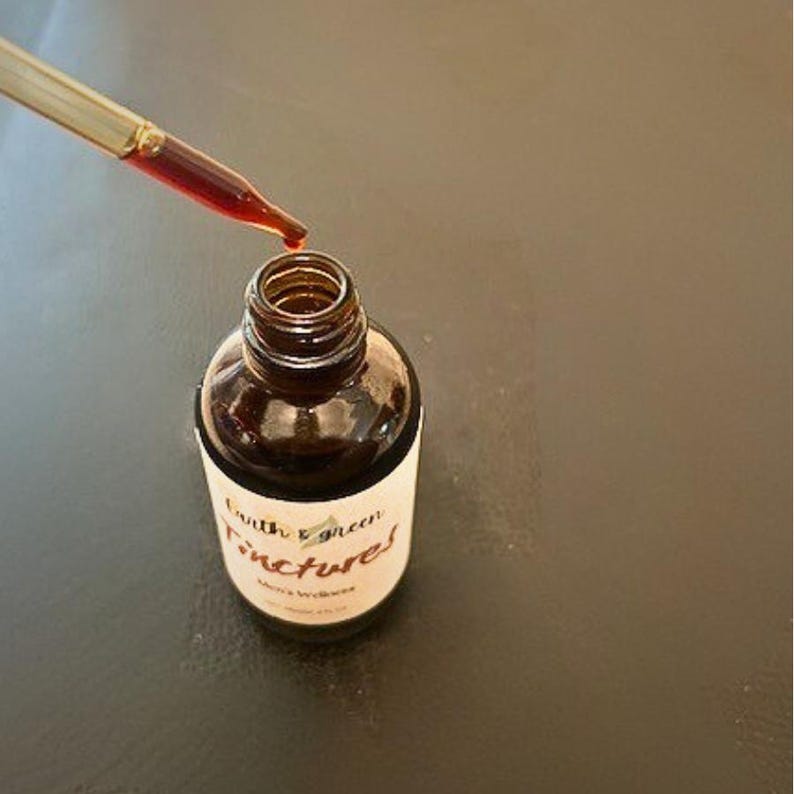 May include: A brown glass bottle labelled "Earth & Green Tinctures" is being filled with a red liquid from a dropper. The bottle sits on a dark surface. The image focuses on the bottle and dropper, highlighting the product.