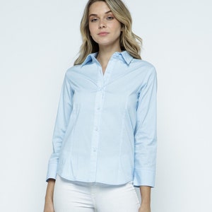 May include: A light blue long-sleeved button-down shirt with a collared neckline. The shirt is tucked into white skinny jeans.