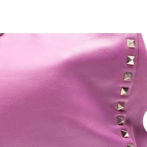 May include: Close-up of a vibrant purple leather handbag. The bag features a row of silver pyramid studs along the edge. The leather has a smooth texture and a slight sheen, creating a luxurious appearance.