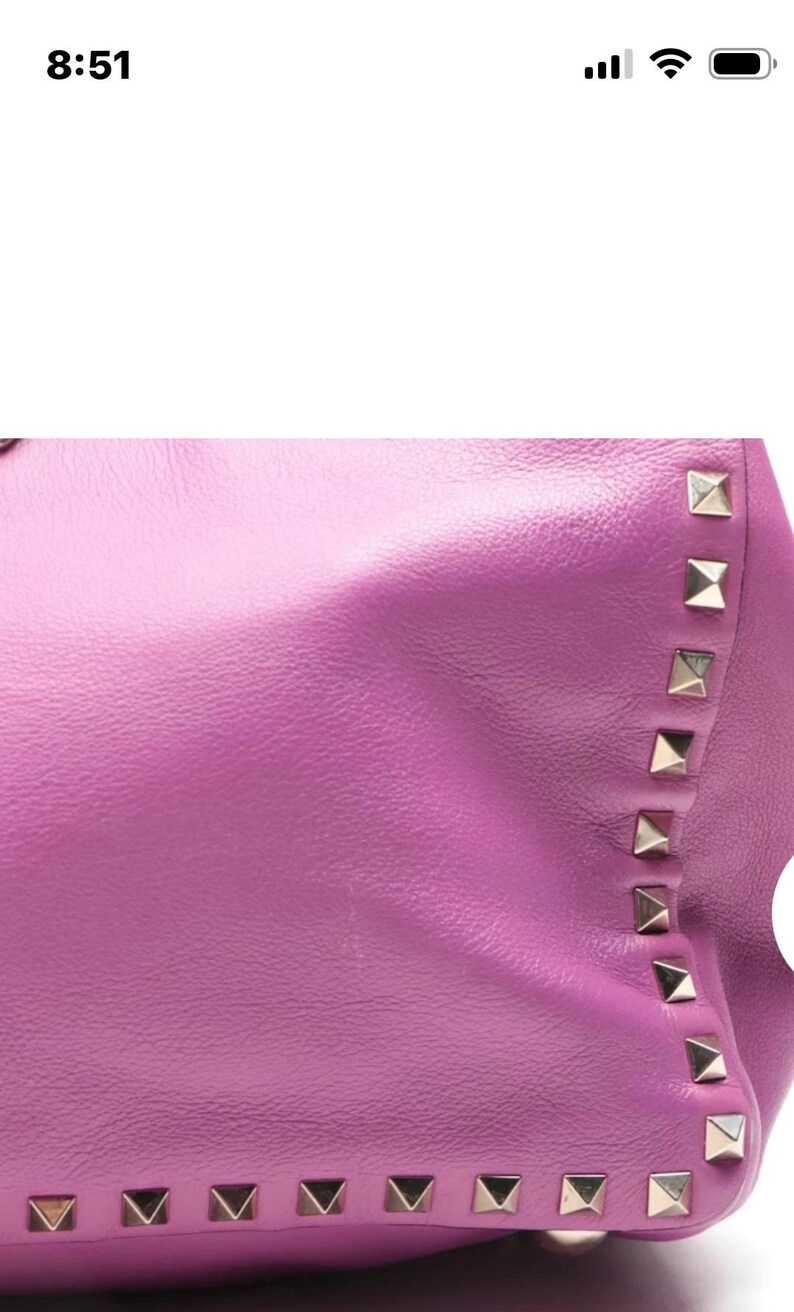 May include: Close-up of a vibrant purple leather handbag. The bag features a row of silver pyramid studs along the edge. The leather has a smooth texture and a slight sheen, creating a luxurious appearance.