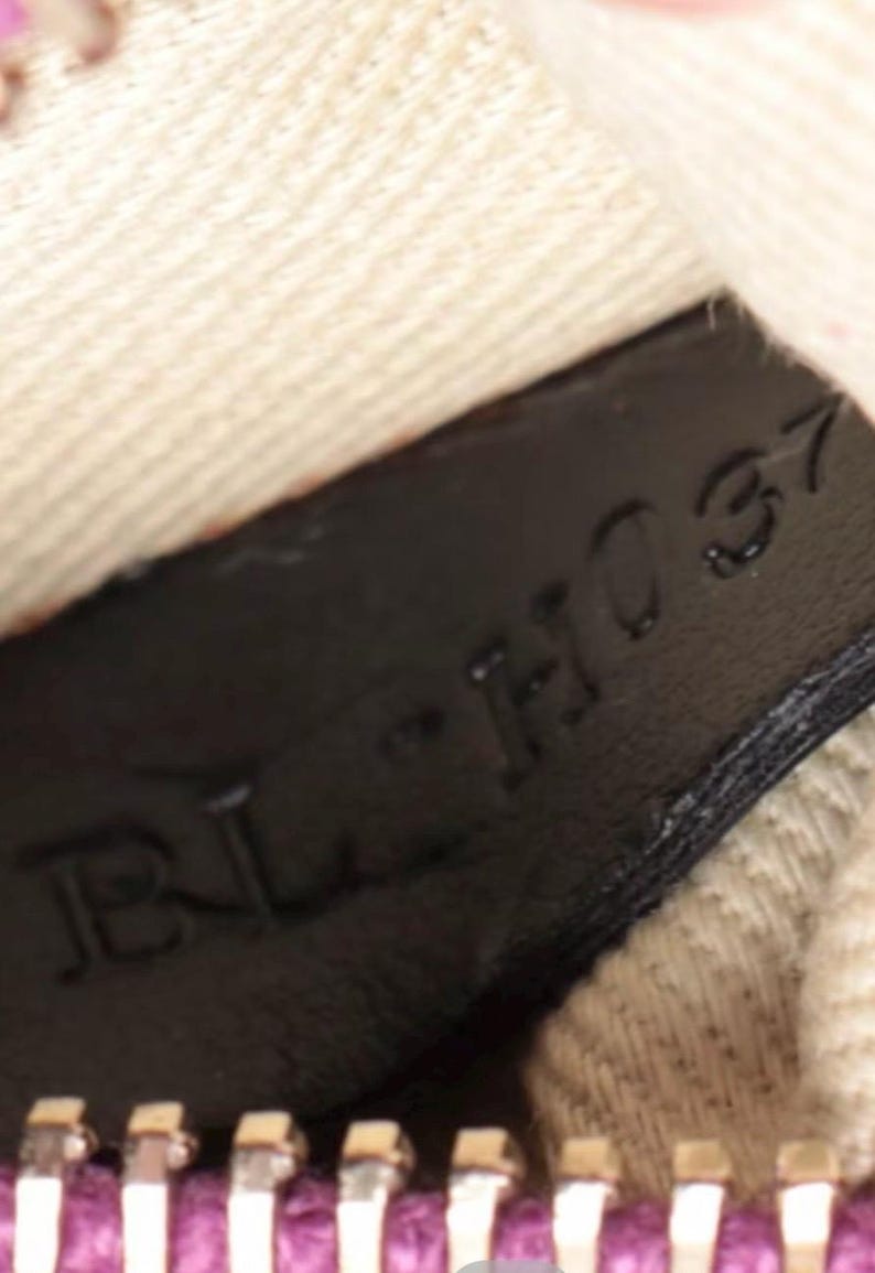 May include: Close-up of a black leather tag with the embossed text "BL-H037". The tag is set against a textured, off-white fabric and a purple zipper.