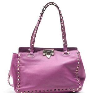 May include: A vibrant purple leather handbag with silver-tone pyramid studs along the edges and straps. The bag features a top handle design, a flap closure, and a structured silhouette, perfect for carrying essentials.