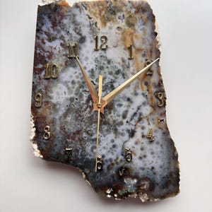 May include: A unique clock with gold hands and numbers set into a natural agate slice. The agate is a mix of brown, white, and gray with a mottled pattern.