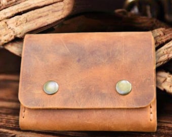 May include: A brown leather wallet with two metal snaps. The wallet has a distressed look and is made of a soft, supple leather.