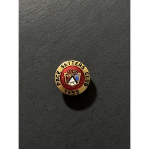May include: A vintage Ford Pace Setters Club pin from 1955. The round pin features a red center with the word "FORD" and a stylized emblem. The outer ring is gold with the words "PACE SETTERS CLUB" and the year "1955".