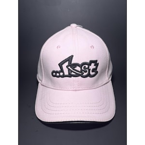 May include: A light pink baseball cap with a curved brim. The cap features the word "Lost" in black, stylized lettering on the front. The hat has a six-panel design with a button on top.