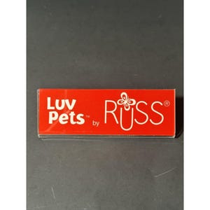May include: A rectangular red sign with the text "Luv Pets" in white, followed by "by" and the name "RUSS" in white, with a butterfly graphic. The sign is in a clear plastic holder.