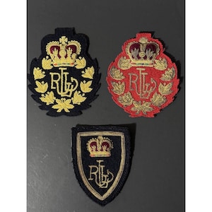 May include: Three embroidered fabric patches featuring the RL logo in gold thread. Two patches are circular with a crown and maple leaf border, one in navy blue and one in red. The third patch is a navy blue shield shape with a crown and RL logo.