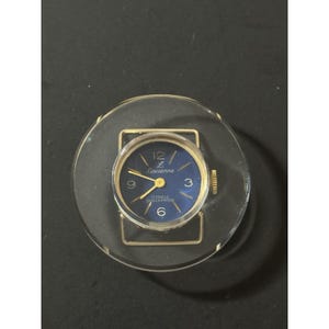 May include: A vintage Lausanne wristwatch with a blue face, gold hands, and gold-tone case. The watch is set in a clear, circular acrylic holder. The watch face displays the numbers 12, 3, 6, and 9.