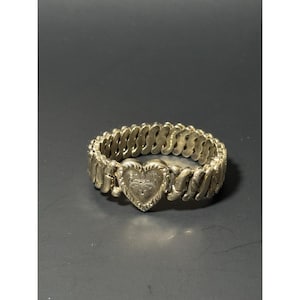 May include: Silver-toned stretch bracelet featuring a heart-shaped centerpiece with an engraved floral design. The bracelet has a flexible, linked band. The heart measures approximately 1 inch wide.