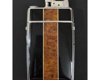 May include: A rectangular lighter with a silver metal frame. The lighter's face features a black background with a vertical stripe of wood grain in the center. The top of the lighter has a silver metal mechanism.