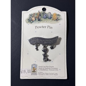 May include: A pewter pin featuring a design from Winnie the Pooh. The pin has a banner with the text "Nobody can be uncheered with a balloon". The pin includes a bunny holding a balloon. The pin is on a white card with the price $19.00.