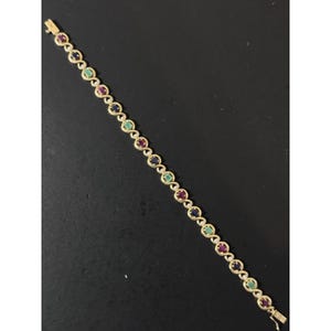 Puede incluir: Una pulsera dorada con piedras preciosas rojas, verdes y azules alternadas. La pulsera presenta un diseño delicado con pequeñas piedras preciosas redondas dispuestas en un patrón repetitivo. El cierre es dorado.