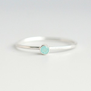 May include: A delicate silver ring with a small, light blue gemstone.