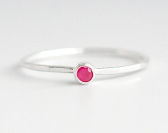 Puede incluir: Un anillo de plata sencillo con una pequeña piedra preciosa redonda de color rosa brillante.