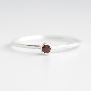 May include: A simple silver ring with a small, round, red gemstone.