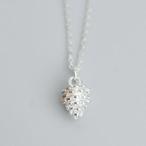 May include: A silver necklace with a small, detailed pine cone pendant.